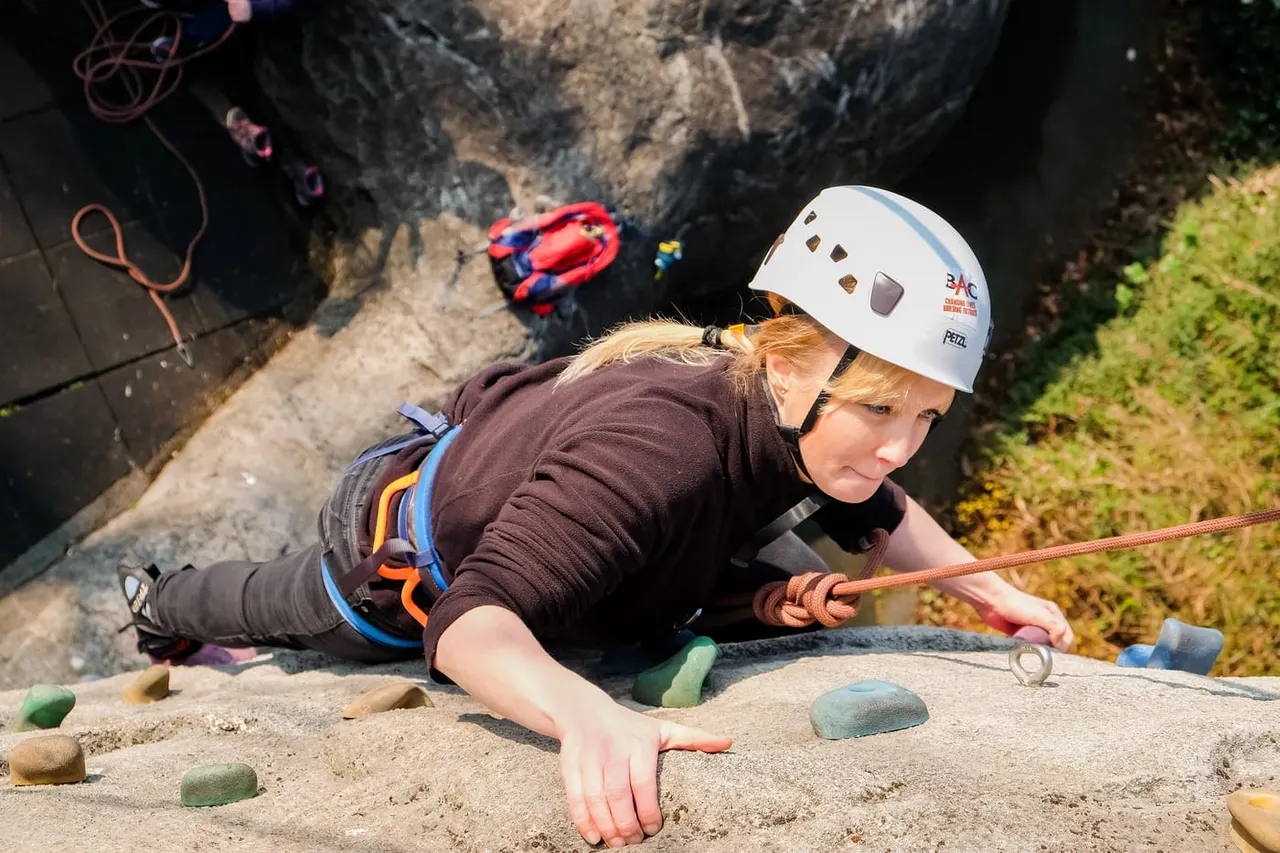 Person rock climbing on an indoor climbing wall with safety equipment and rope.