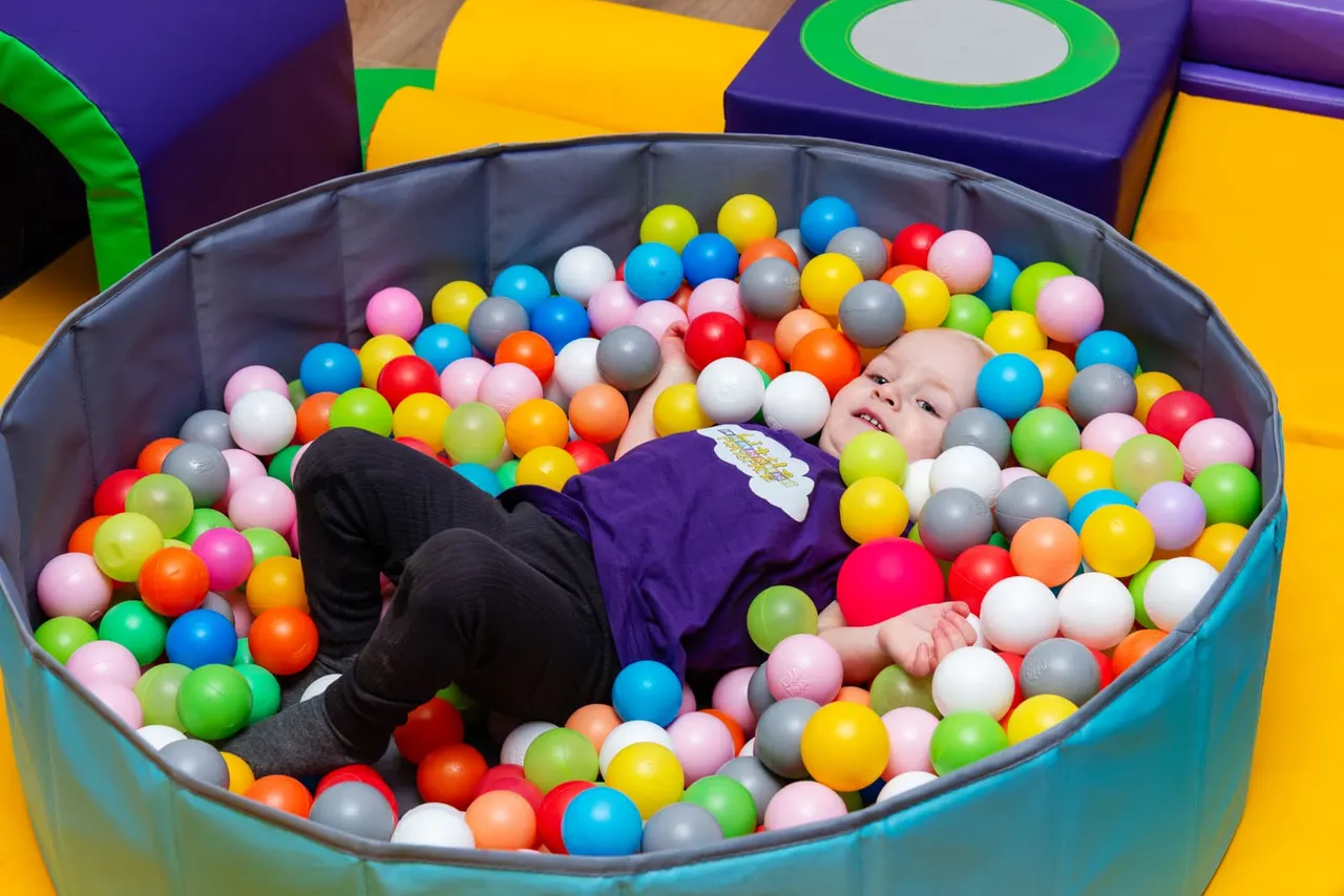 Young child playing in a ball pit filled with colourful plastic balls at an indoor play centre.