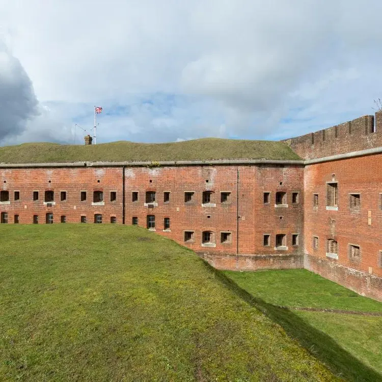 Interior courtyard of a historic brick fortress with grass-covered ramparts and a British flag flying above.