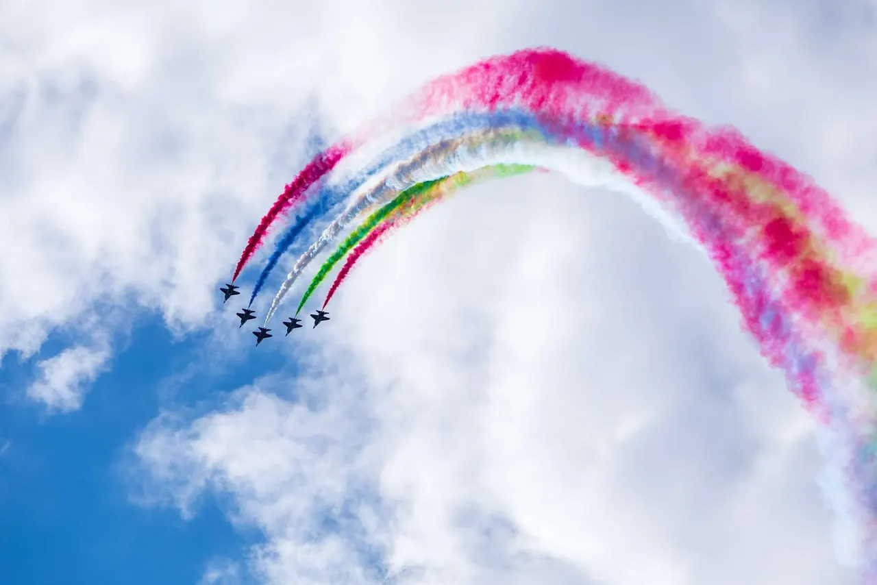 Five military aircraft performing a loop formation with coloured smoke trails against a blue sky.