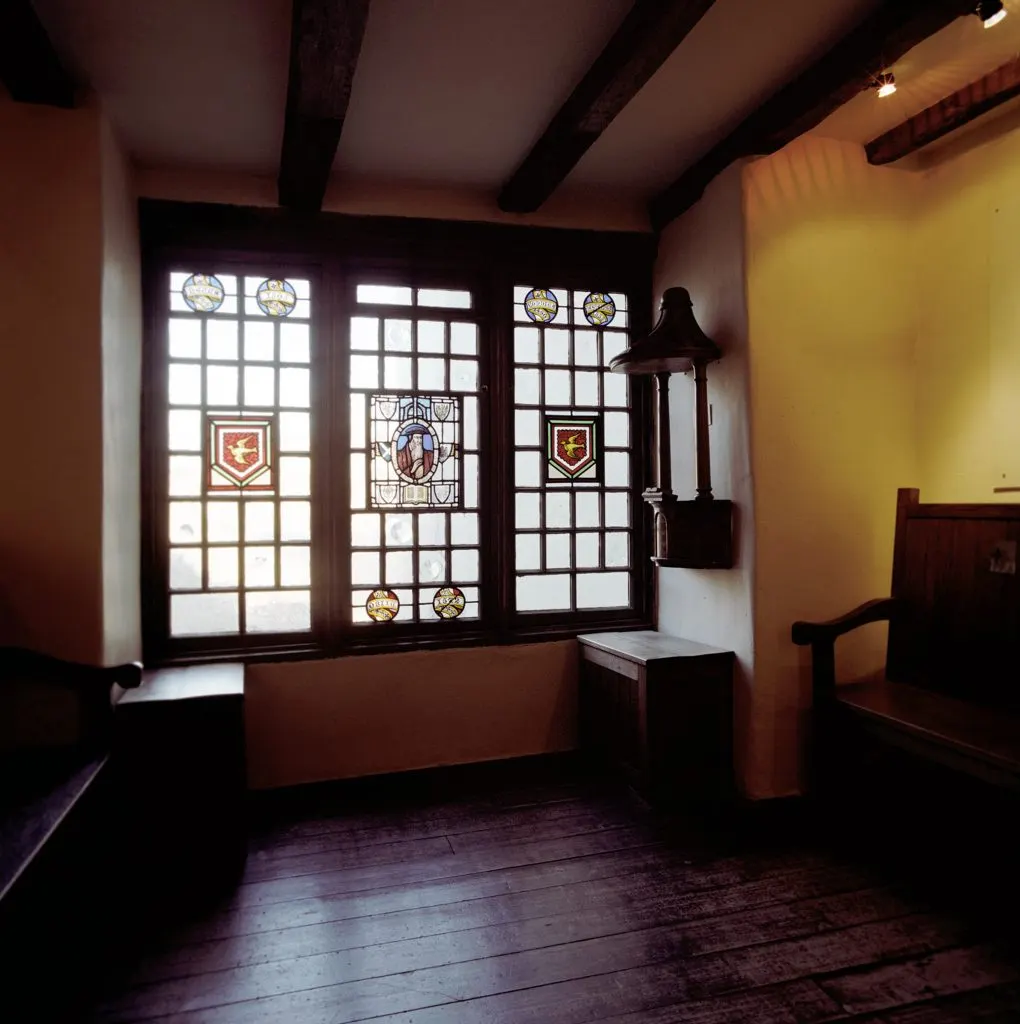 Interior room with leaded stained-glass windows, wooden beams, and period furnishings in historic setting.