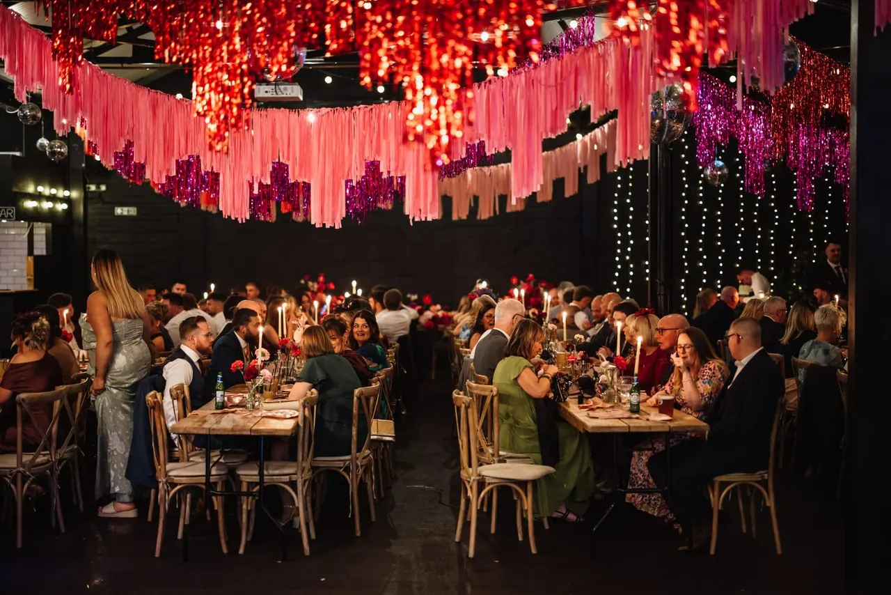 Formal dinner event with guests seated at tables under dramatic red and purple illuminated ceiling installations with hanging decorations.