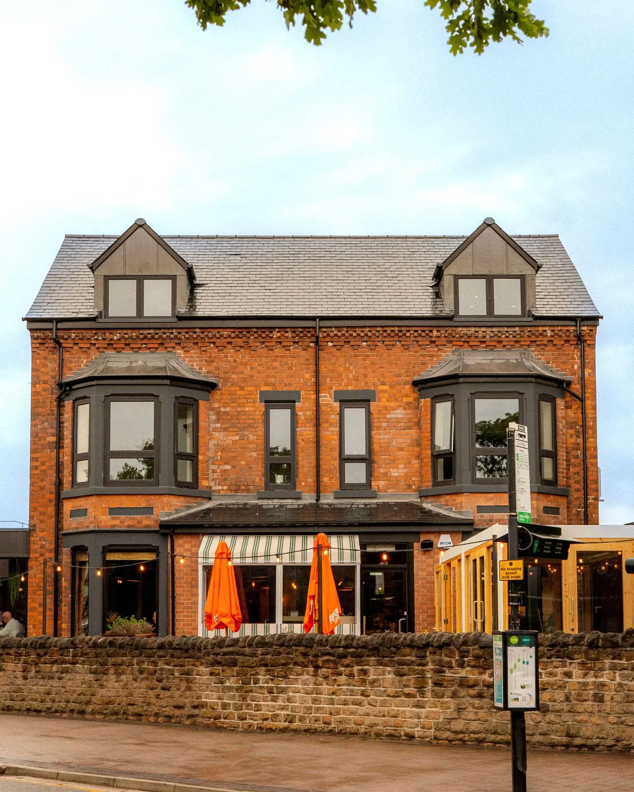 Red brick building with orange umbrellas on the outdoor terrace, housing a pizza restaurant on the ground floor.
