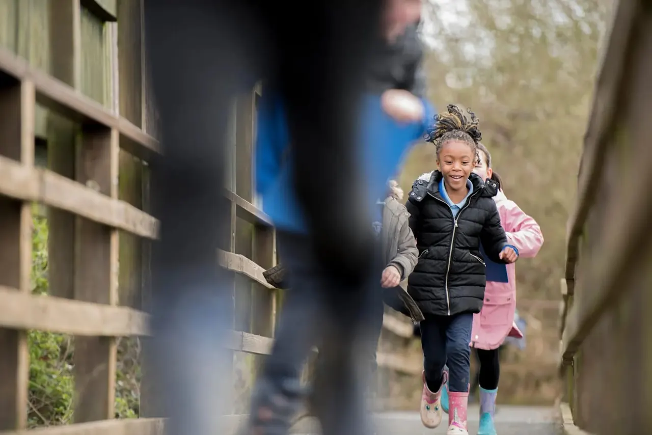 Children running through a narrow stone-walled alleyway on a countryside path.