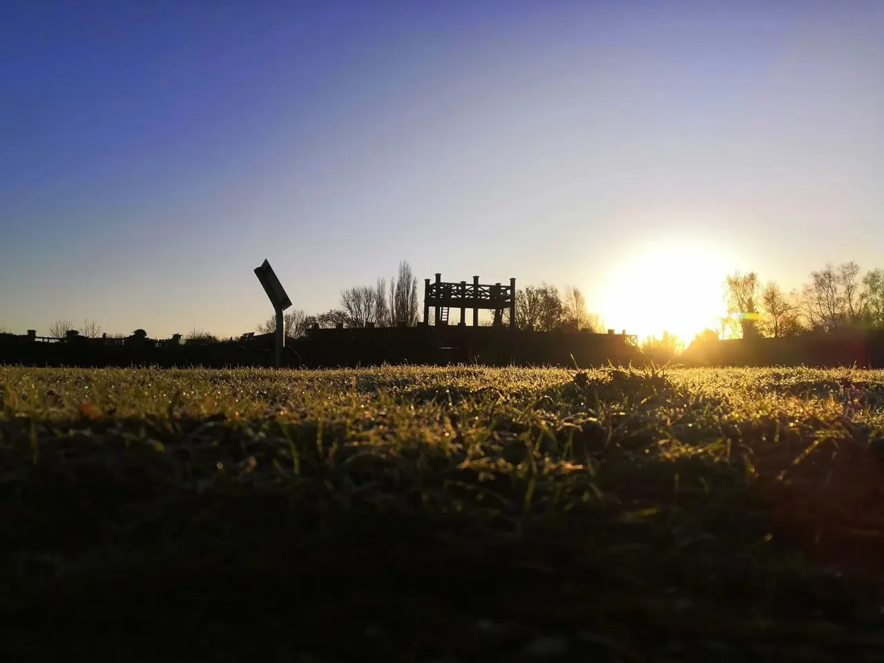 Silhouetted Roman fort structure and reconstructed siege equipment at sunset across an open grassland.