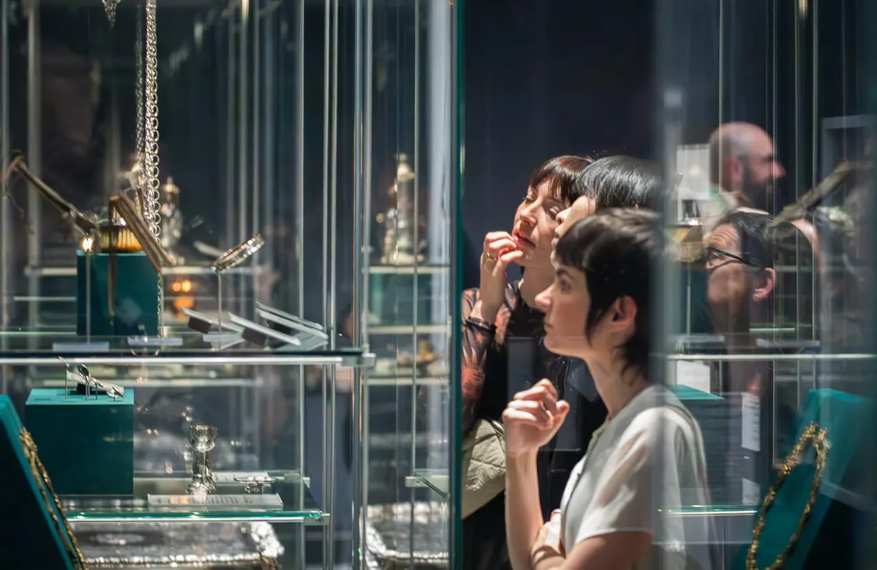 Visitors viewing jewellery and decorative objects displayed in glass cases in a museum gallery.