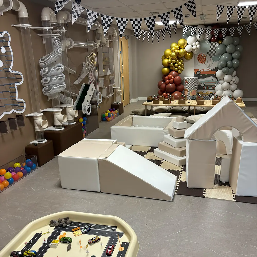 Indoor play area with racing-themed décor, soft play structures, ball pits, toy cars and checkered bunting.
