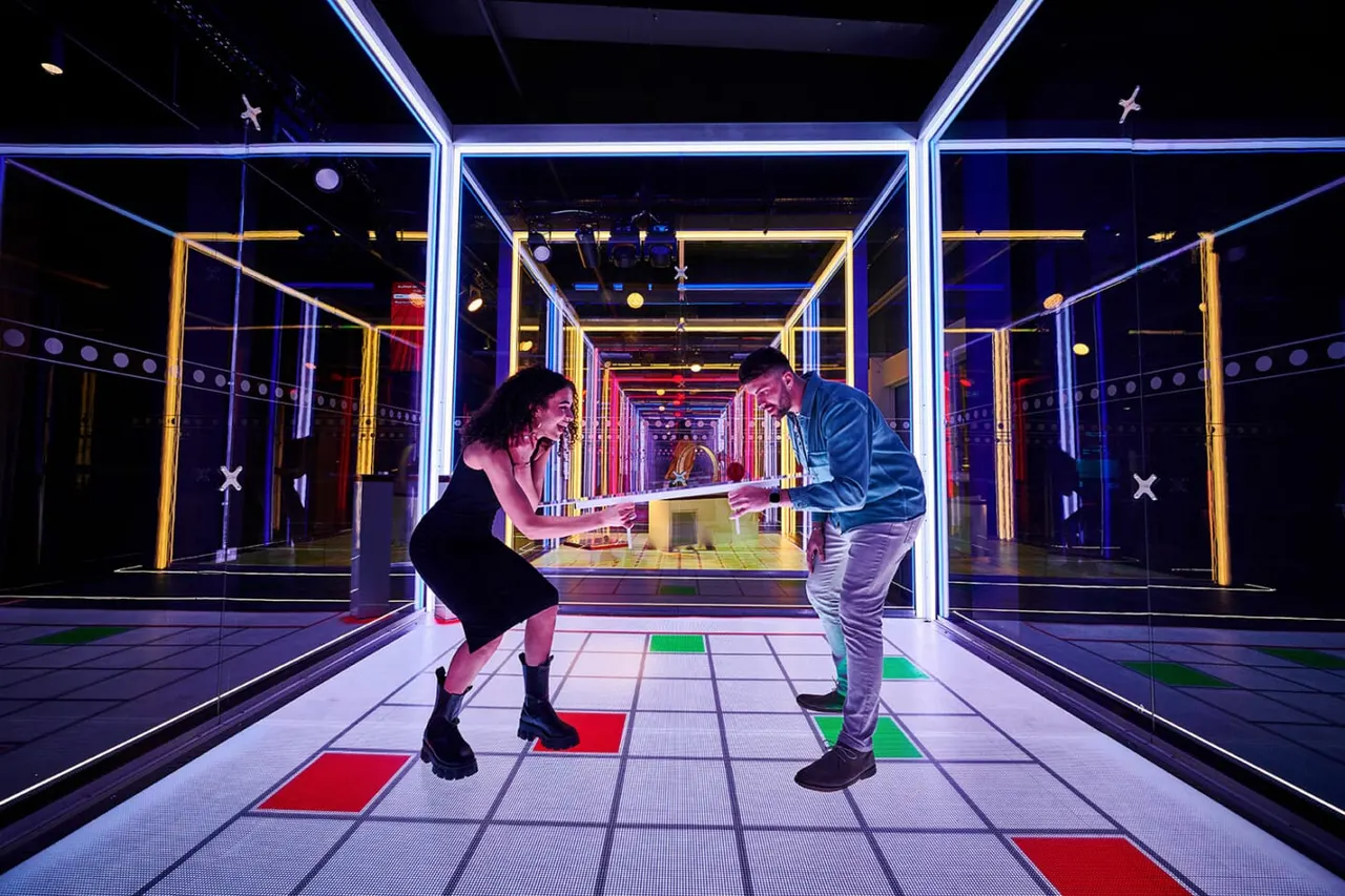Two people playing interactive digital mini golf in a neon-lit corridor with glowing blue and gold framed walls.