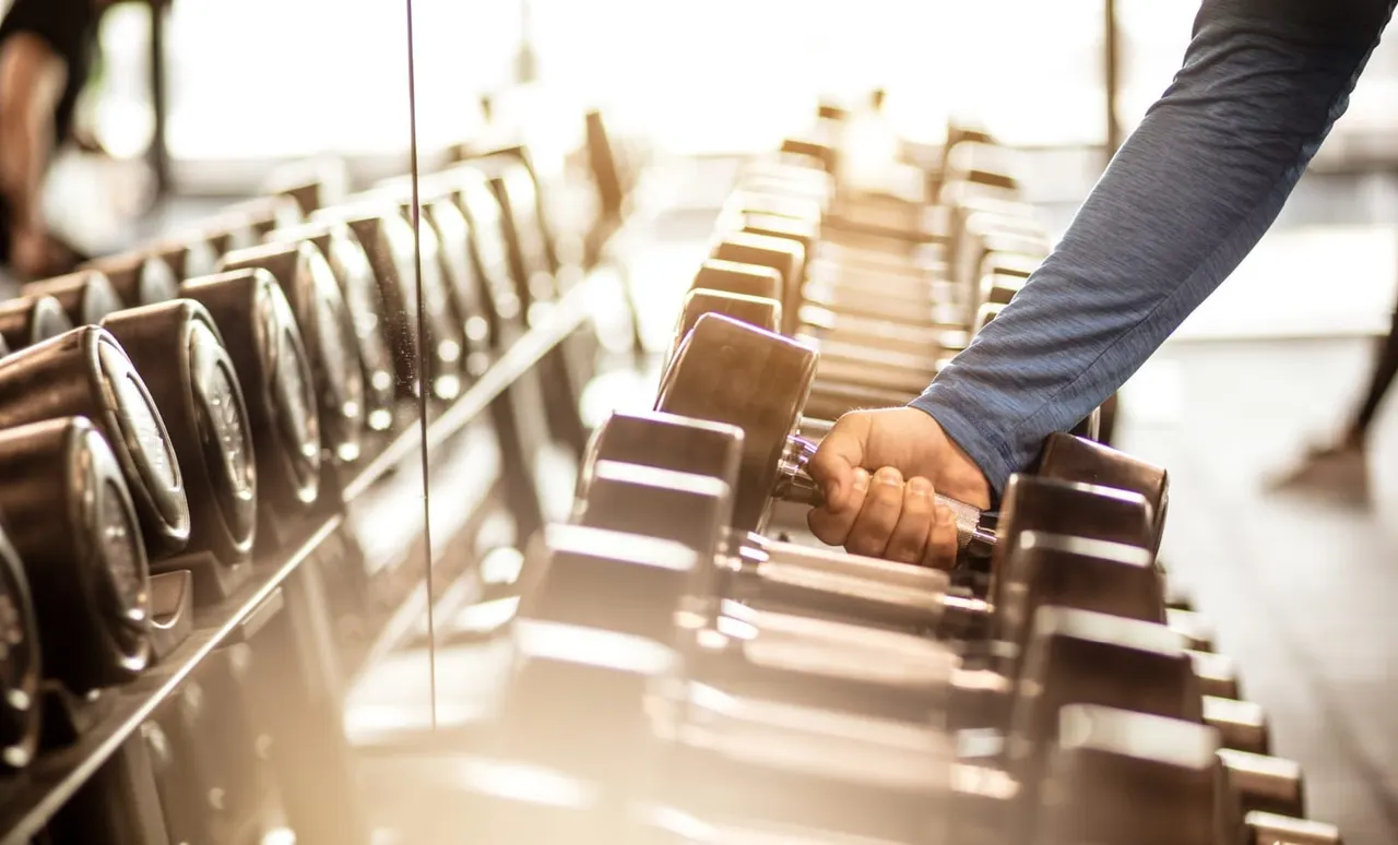 Person selecting a dumbbell from a rack during a gym workout session.