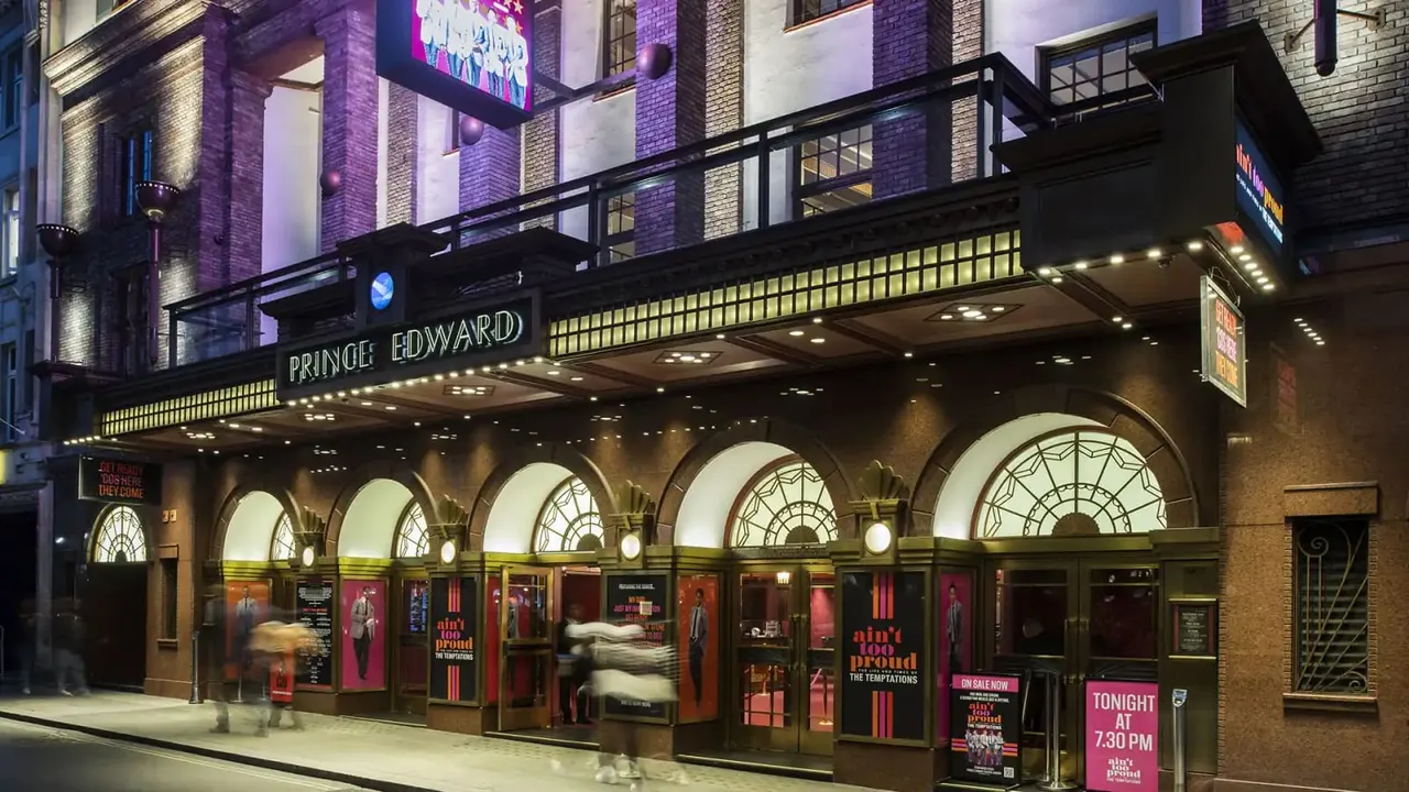 Historic theatre building facade illuminated at night with ornate arched windows, marquee signage and red entrance doors.