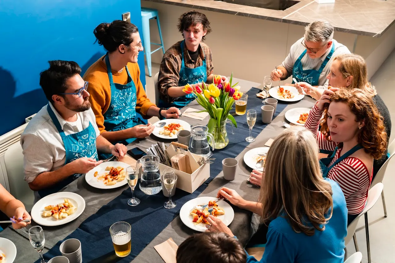 Group of adults and children dining together at a table with plated food, drinks, and a flower arrangement, with staff members in aprons serving.