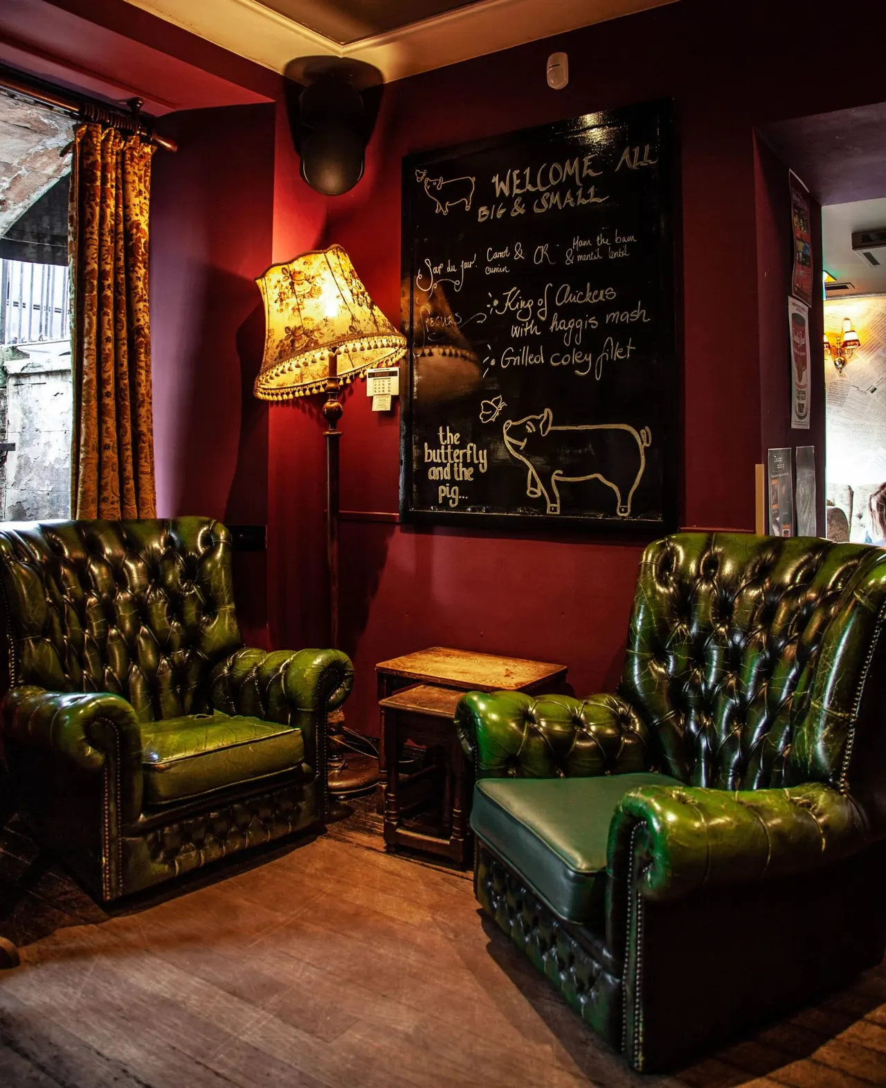 Interior seating area with green leather chesterfield chairs, burgundy walls, and a menu board advertising food offerings.