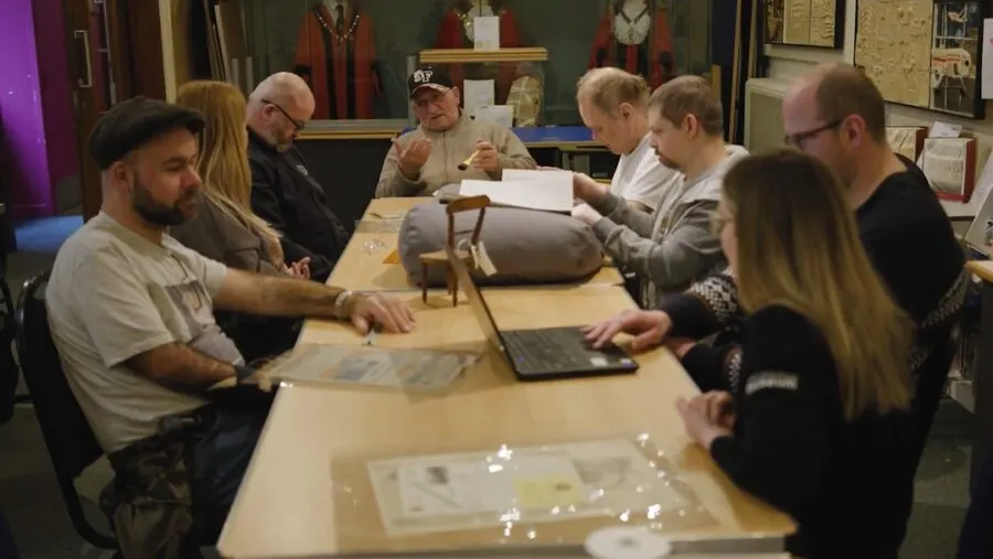 A group of adults gathered around a wooden table examining documents and artefacts during a museum workshop or educational session.