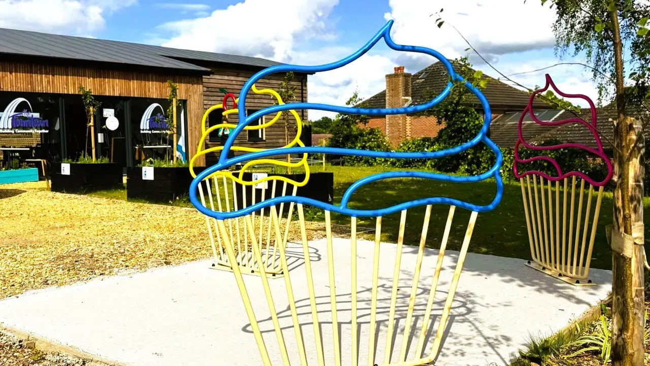 Colourful metal climbing structure in outdoor leisure venue with modern buildings and green lawn behind.