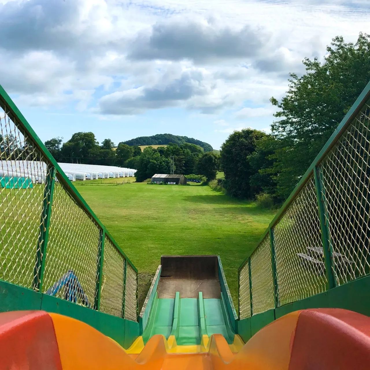 View down a colourful slide towards a green countryside landscape with trees, fields and farm buildings.
