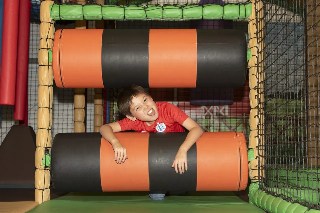 Young child in red shirt crawling through an inflatable obstacle course tunnel with orange and black sections.