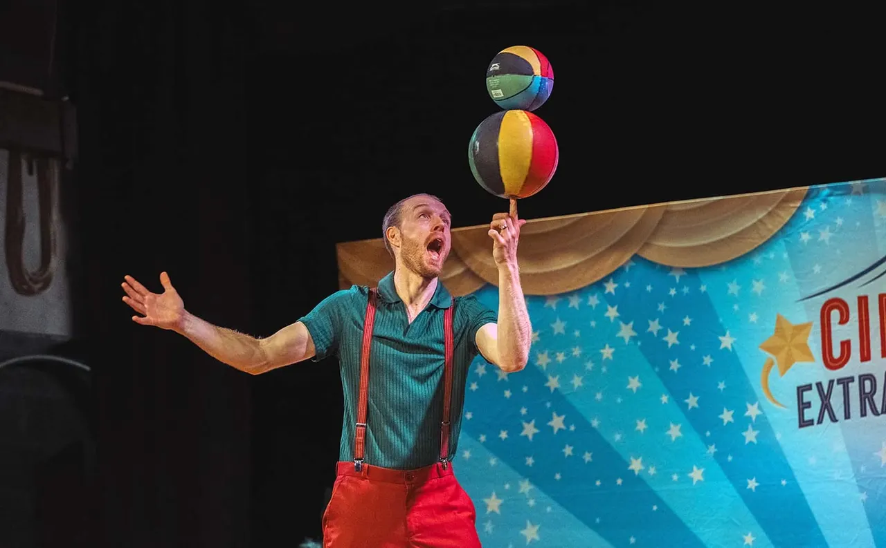Performer spinning stacked coloured balls on one finger during a circus act on stage.