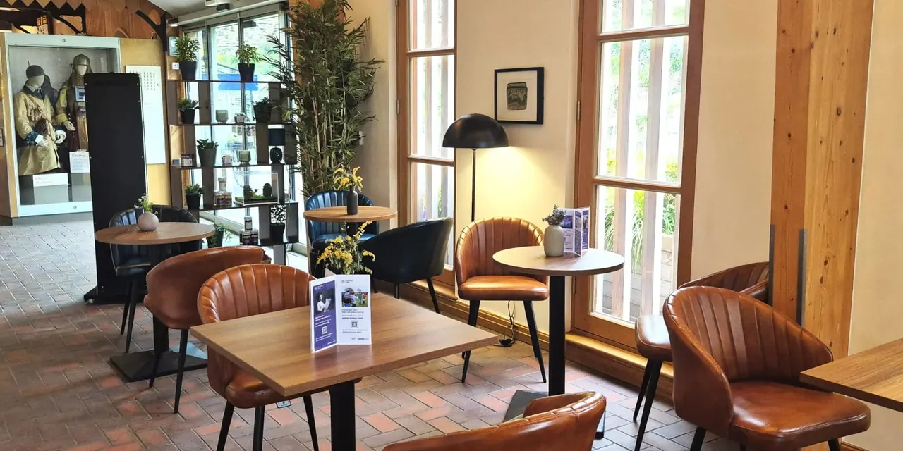 Contemporary interior lounge space with brown leather chairs, wooden tables, potted plants and large windows overlooking gardens.