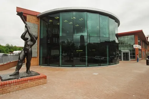 Modern brick and glass library building with curved architecture and abstract sculpture in forecourt.
