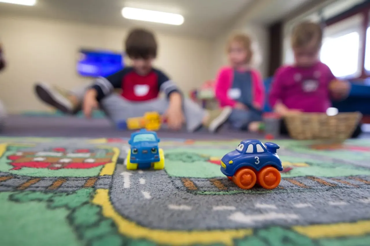 Young children playing with toy cars on a road mat in an indoor play area.