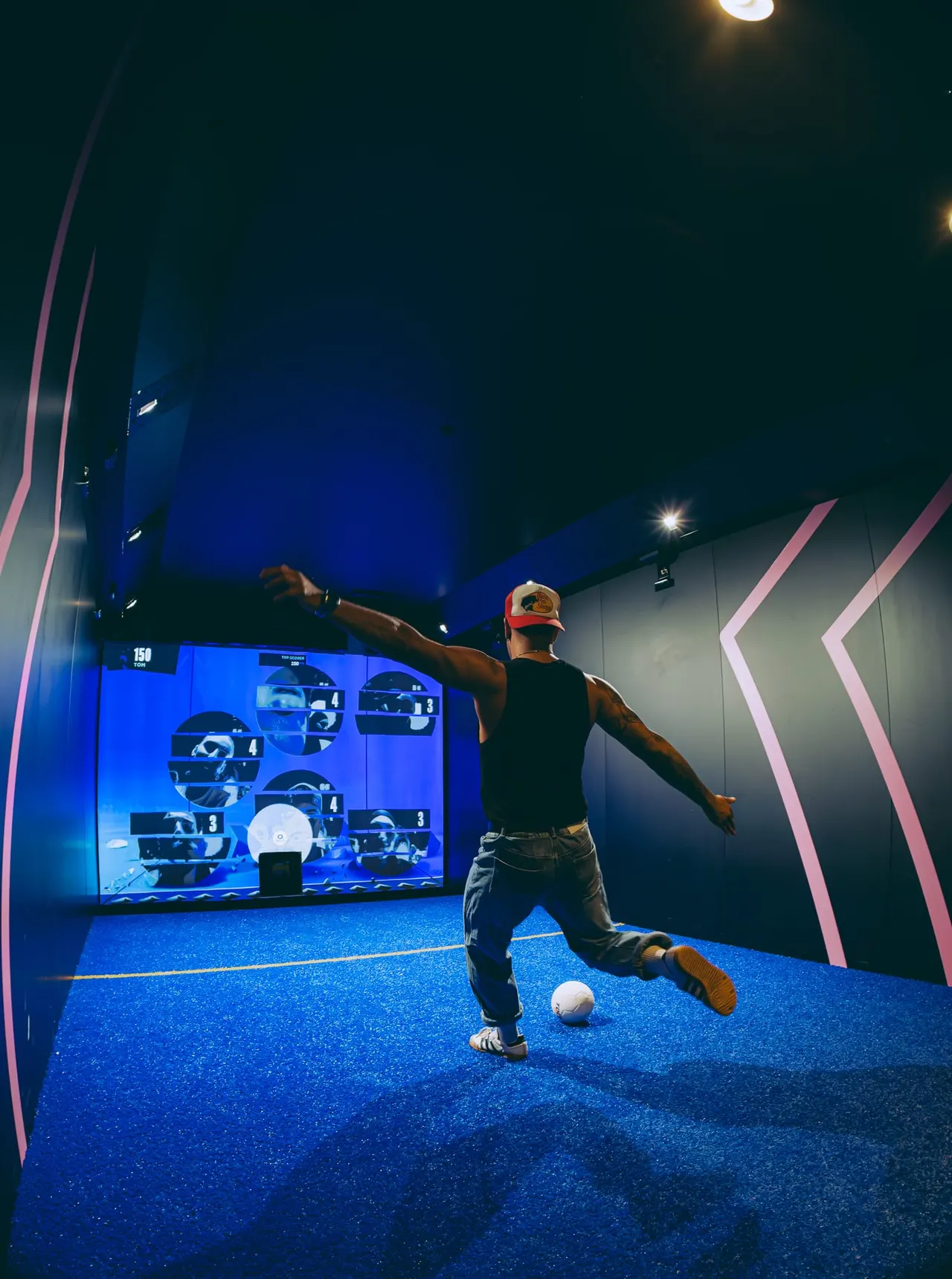 Man playing football in a high-tech indoor venue with blue flooring and interactive screens.