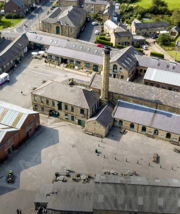 Aerial view of stone buildings and courtyard at former industrial heritage site surrounded by residential properties.