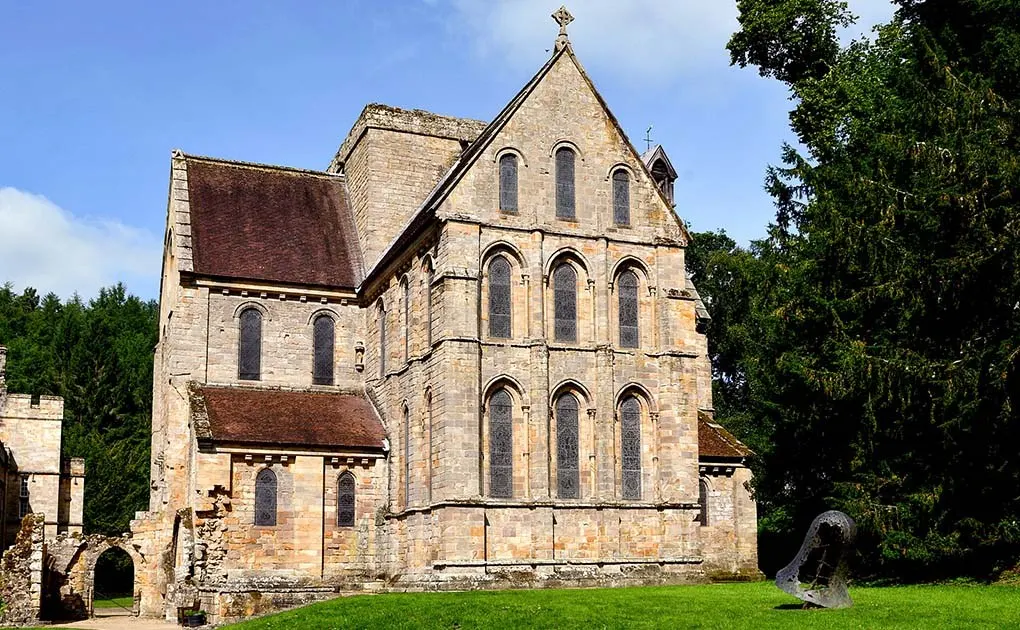 Historic stone church with pitched roof and multiple arched windows, surrounded by green lawns and trees.