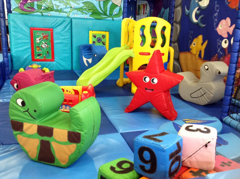 Colourful soft play area with themed foam toys including a turtle, starfish and fish characters, a slide, and number blocks.