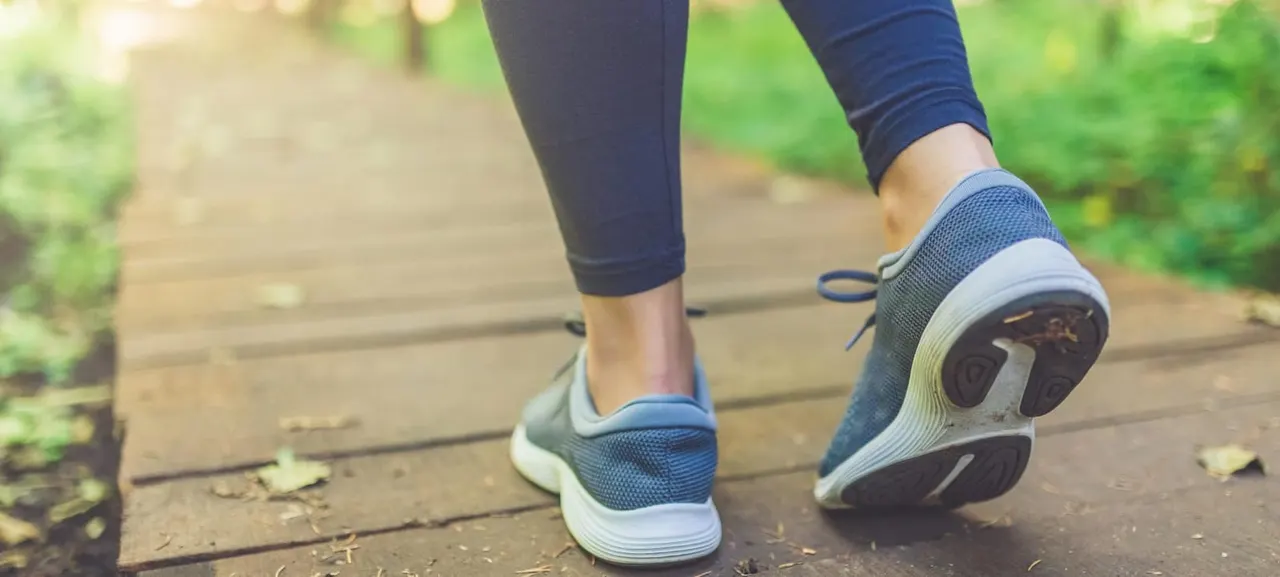 Person jogging on a wooden pathway in dark leggings and blue trainers, surrounded by greenery.