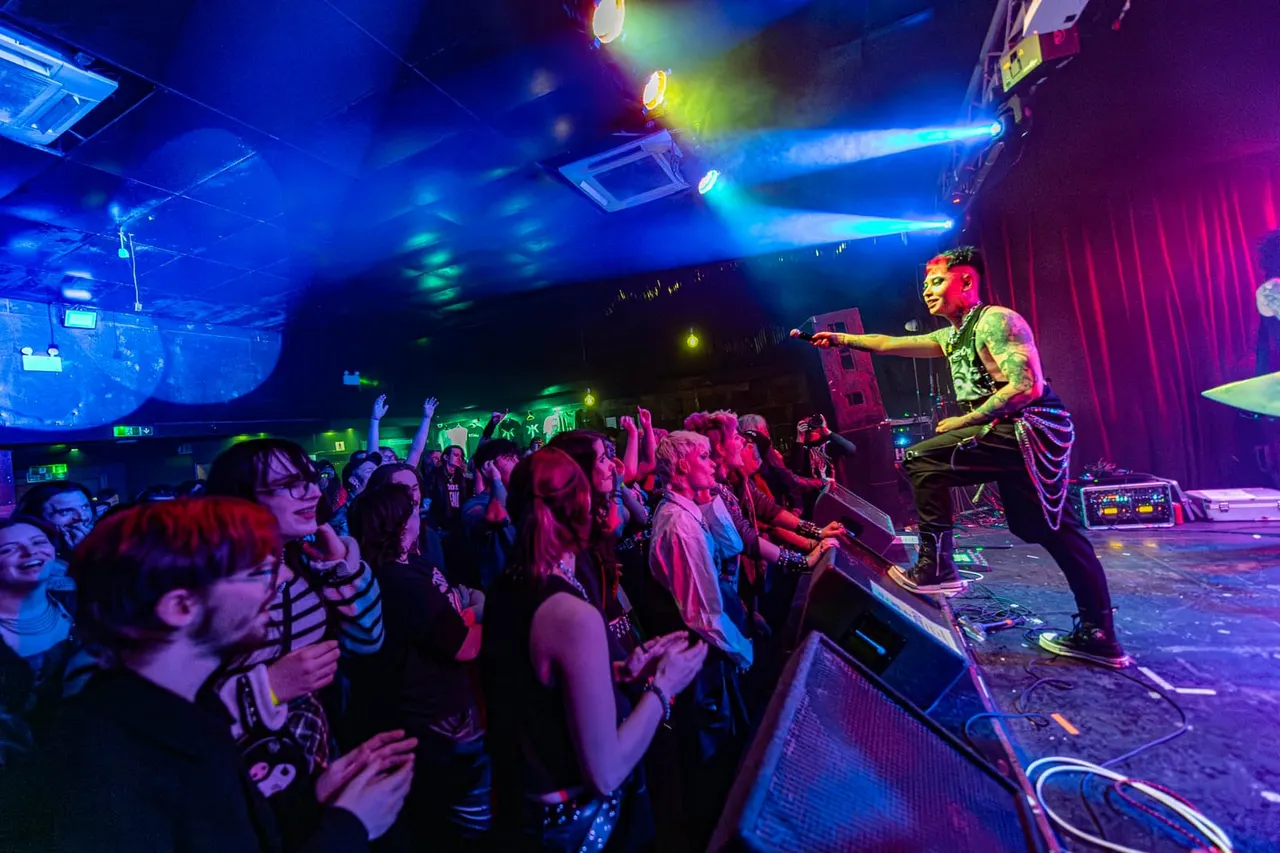 Performer on stage engaging with an enthusiastic crowd under colourful stage lighting at a nightclub venue.
