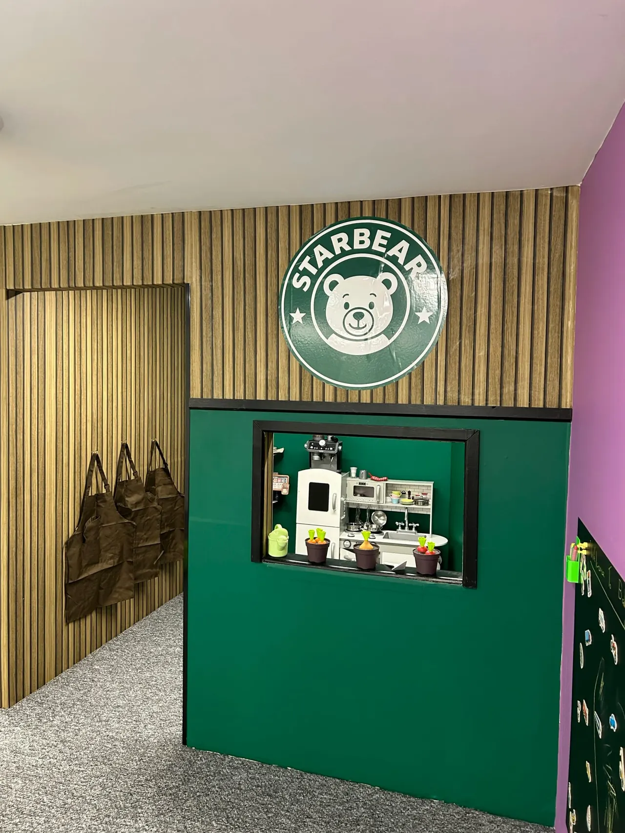 Interior of children's play area with green Starbear-themed cubicle featuring toy kitchen display and bear logo signage.