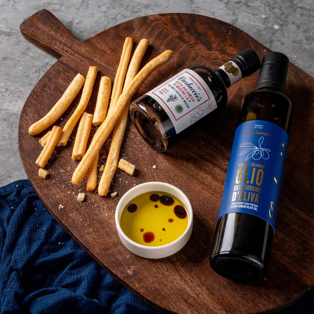Breadsticks, olive oil dipping bowl and wine bottles arranged on a wooden board.