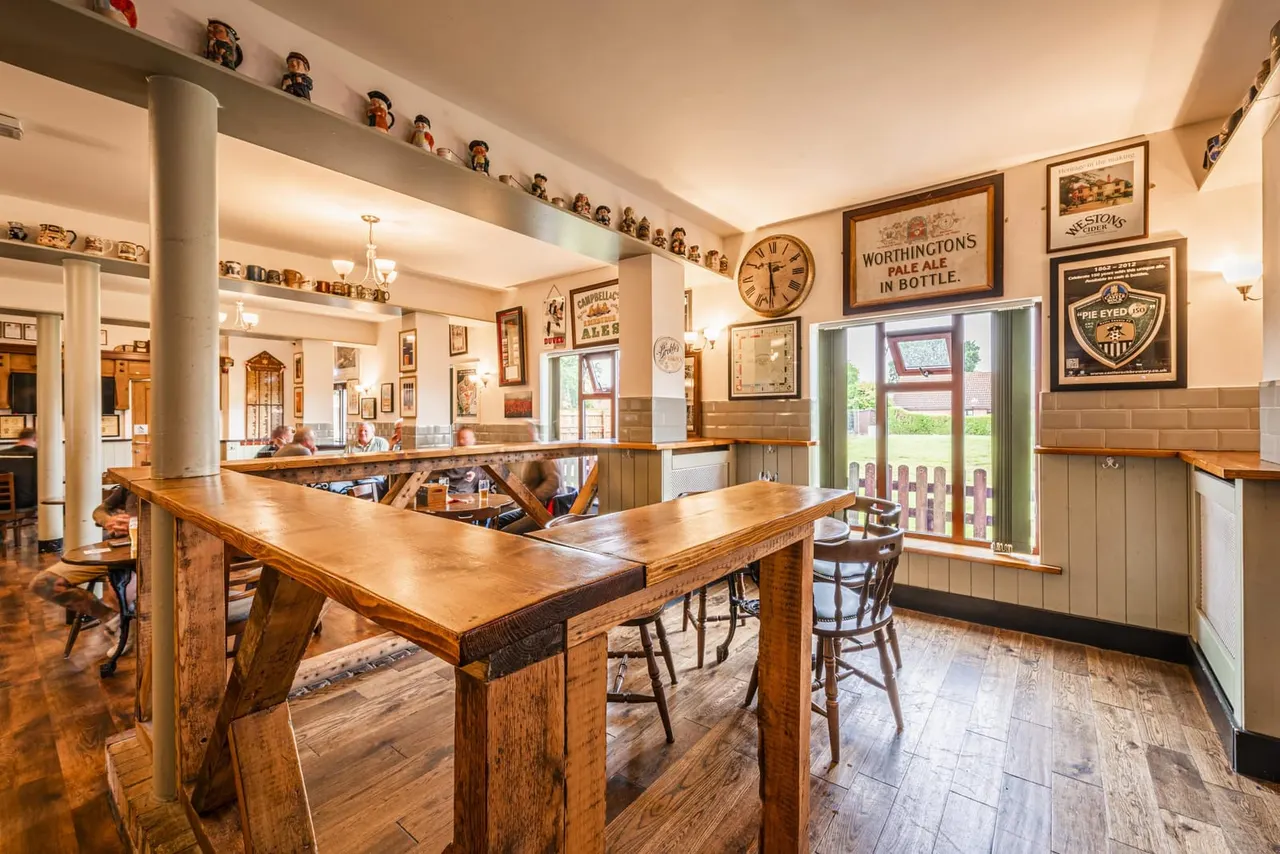 Interior of a traditional pub with wooden bar counters, vintage brewery signs on walls, and shelves displaying collectables.