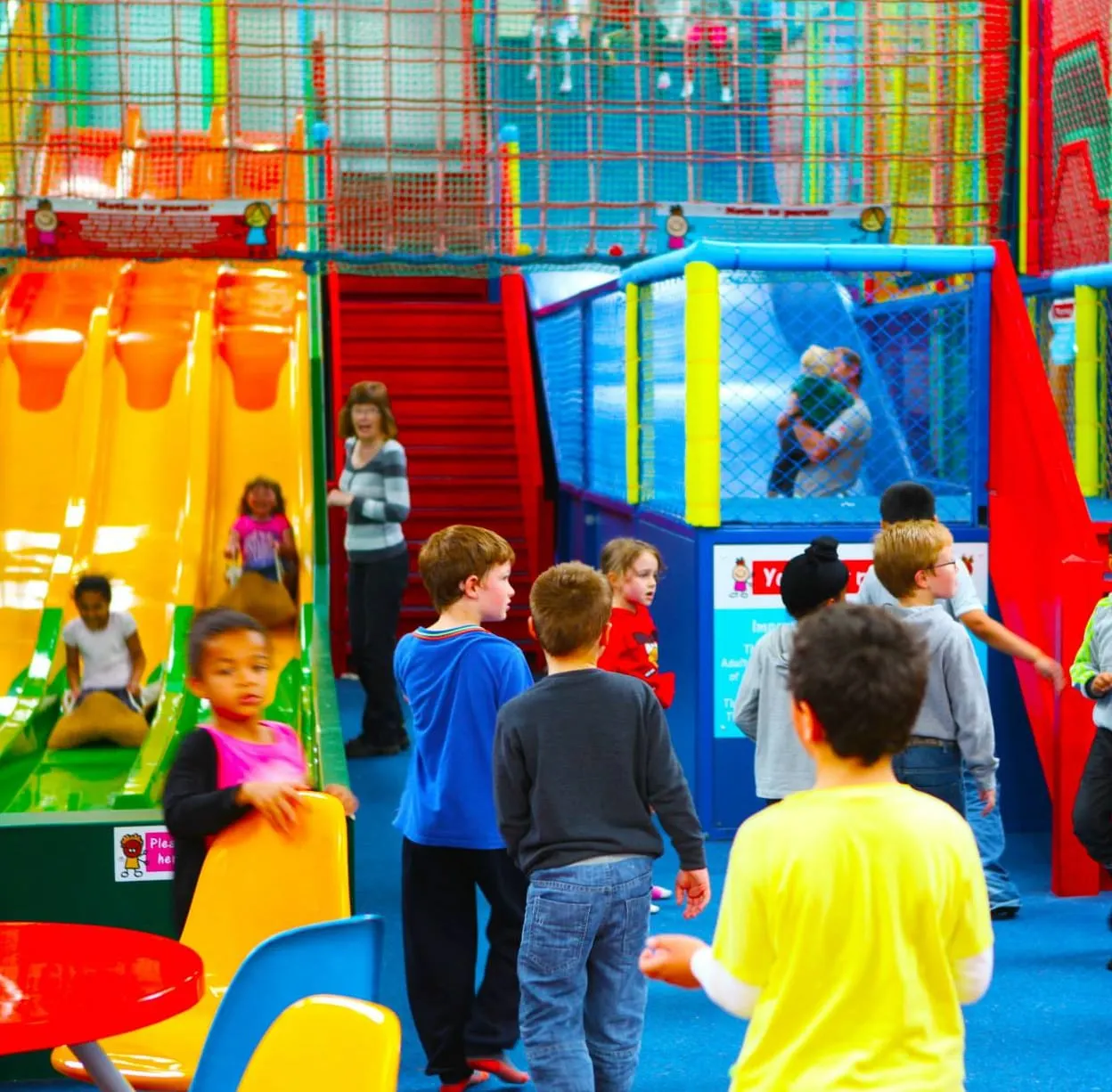 Children playing in a colourful indoor soft play arena with slides, climbing frames and ball pits.