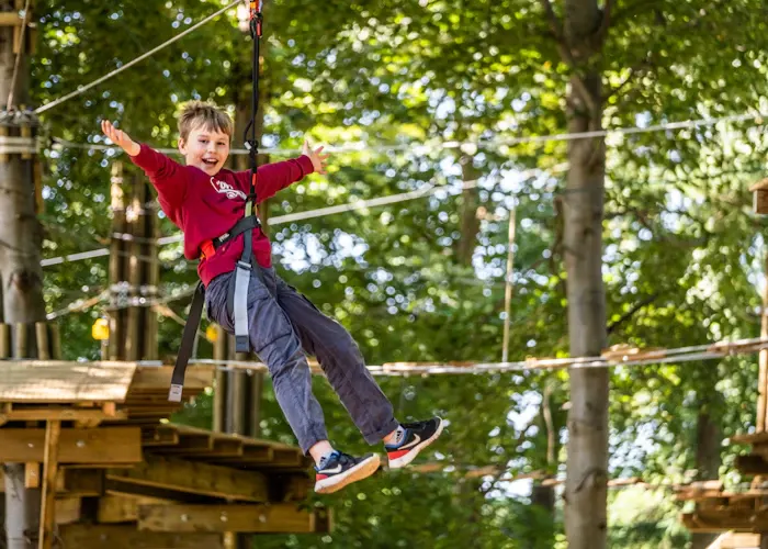 Young child in red jacket flying through the air on a zip line in a woodland adventure course.