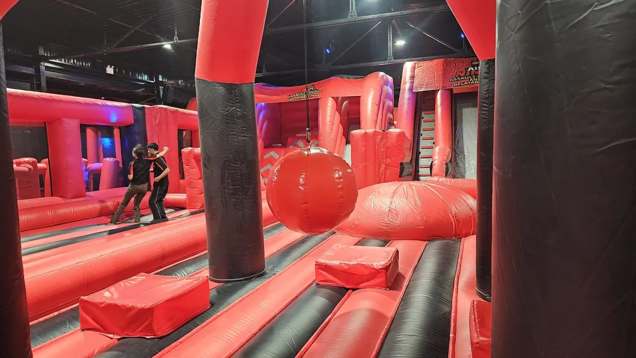 Children navigating through a red inflatable assault course with various obstacles and climbing challenges indoors.
