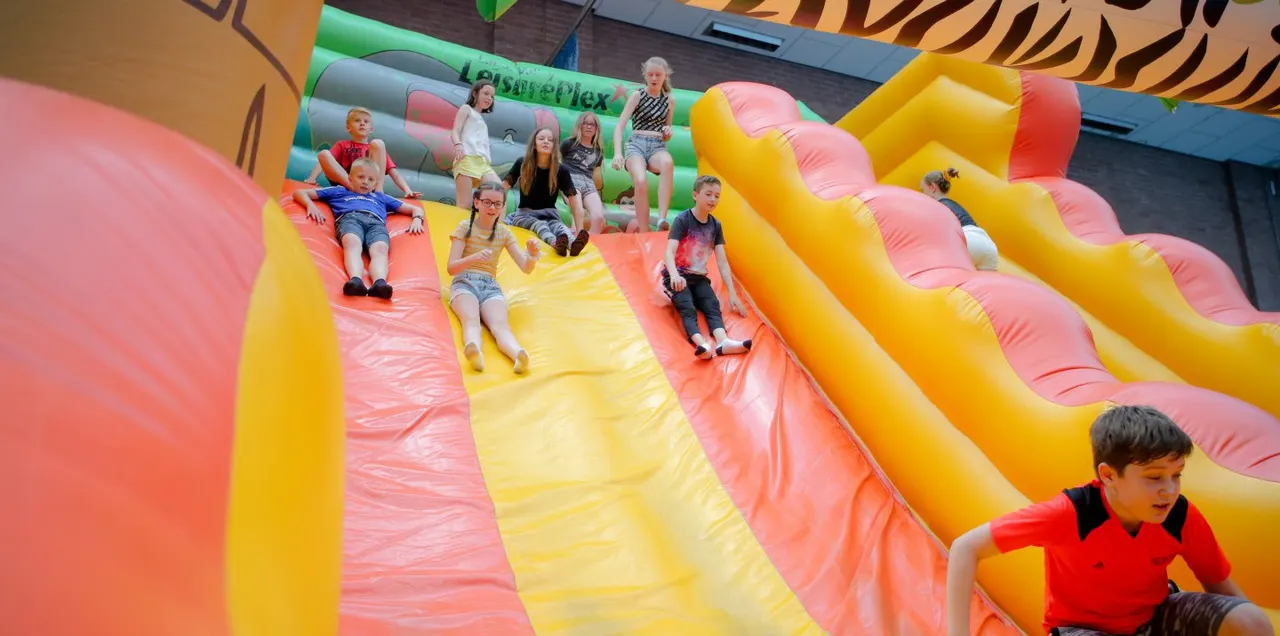 Children sliding down and playing on a large inflatable bouncy castle with multiple coloured slides indoors.