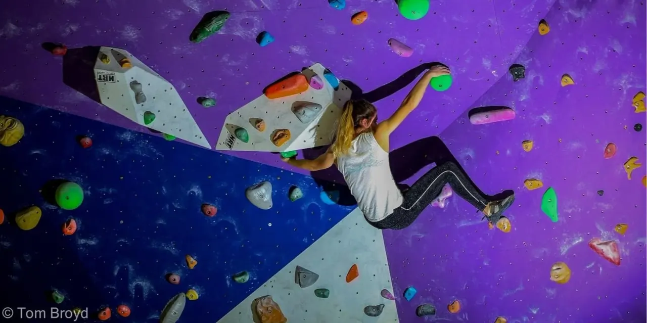 Woman indoor rock climbing on a purple and blue wall with colourful holds.