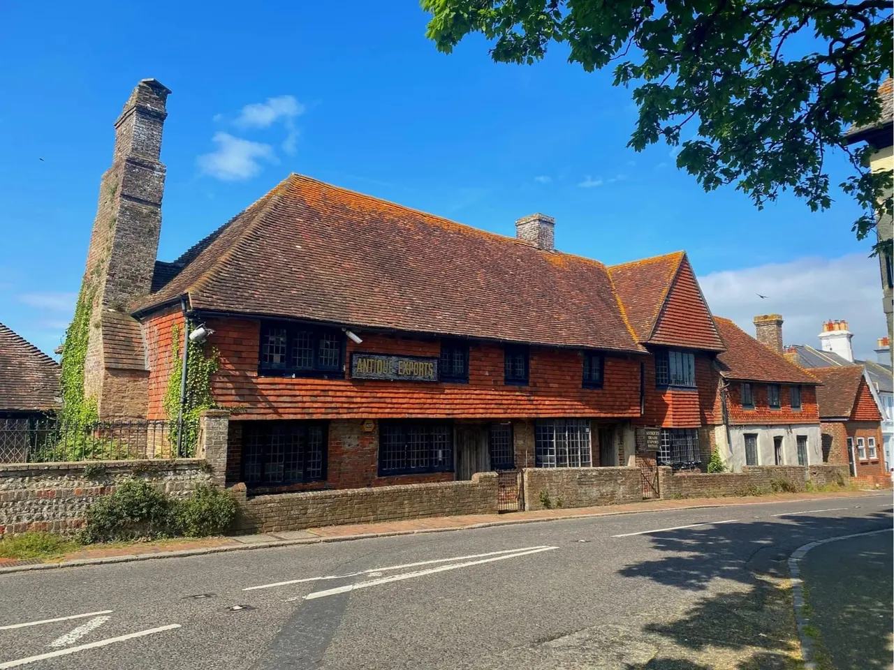 Historic red-brick building with tiled roof and tall chimney, fronted by a street and clear blue sky.