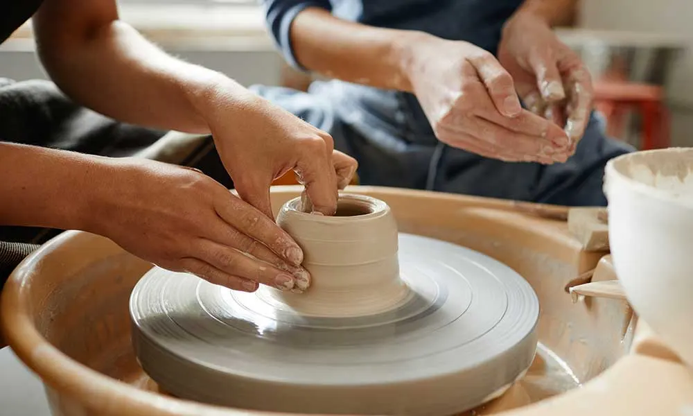 Two people shaping clay on a pottery wheel during a hands-on ceramics workshop.