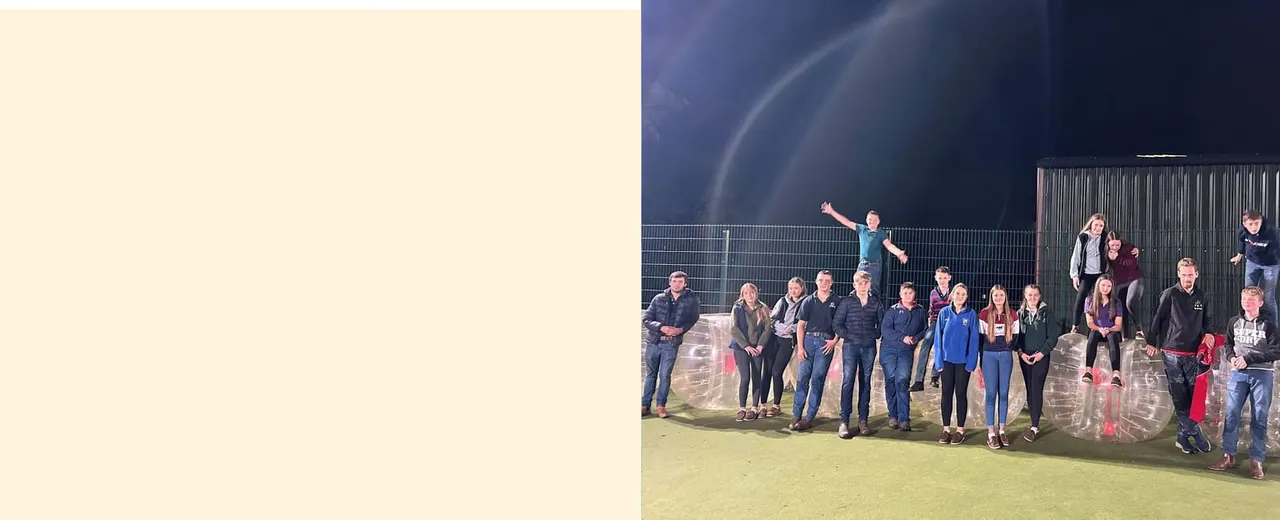 Group of people standing on an illuminated sports field at night, one person elevated on equipment with arms outstretched.