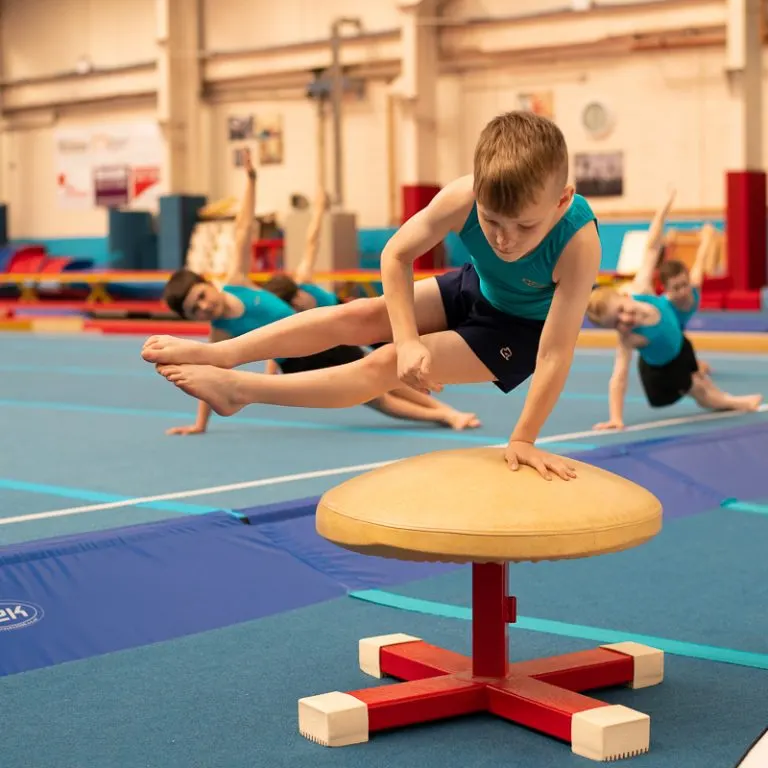 Young gymnasts practising balance and flexibility exercises on apparatus in an indoor gym.