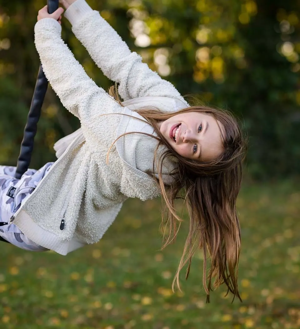 Child swinging upside down on a rope swing with blurred garden foliage in background.