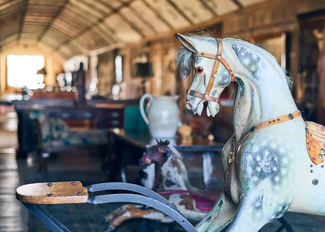 Decorative painted horse sculpture with leather harness inside a stable building.