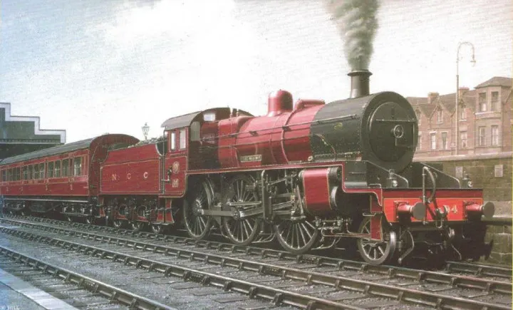A red steam locomotive with passenger carriages at a railway station, circa early 20th century.