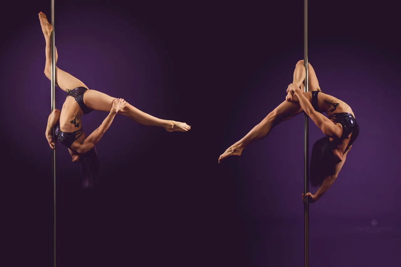 Two pole dancers performing synchronized acrobatic moves on vertical poles against a purple background.