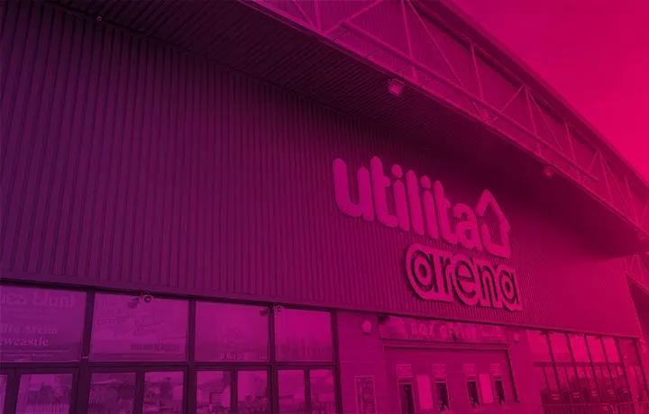 Exterior of a sports arena at night lit in vibrant pink and magenta, showing the "Utilita Arena" signage on the corrugated metal building.
