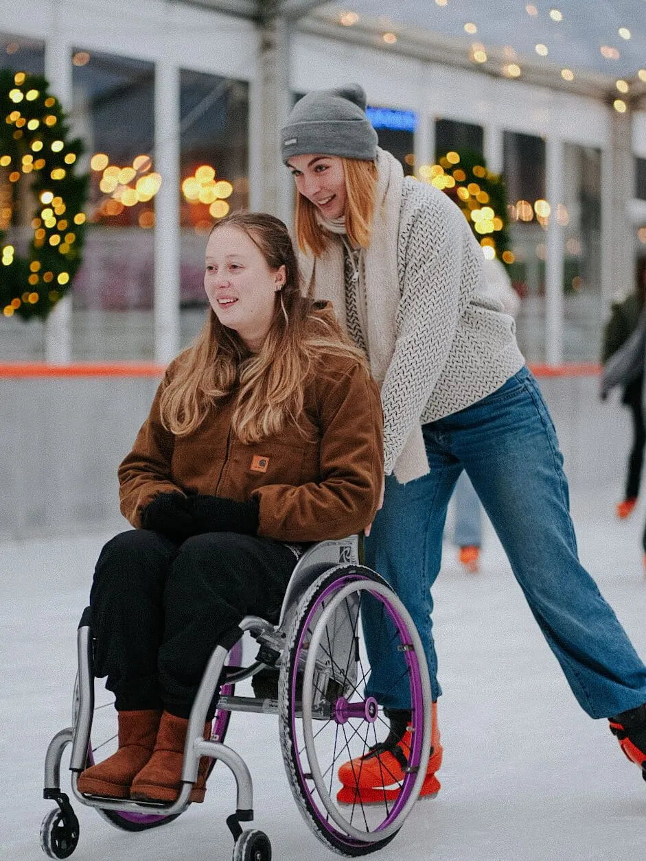 Two people enjoying ice skating at an outdoor rink decorated with festive lights and garland.