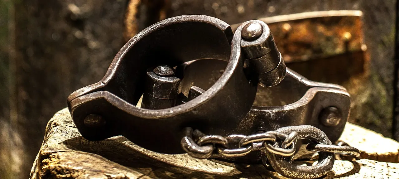 Close-up of a heavy metal shackle and chain on weathered wood, displaying restraint equipment from a historical prison.