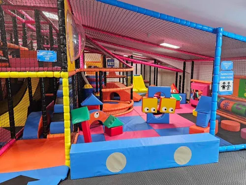 Colourful indoor soft play area with foam blocks, slides and climbing structures for young children.